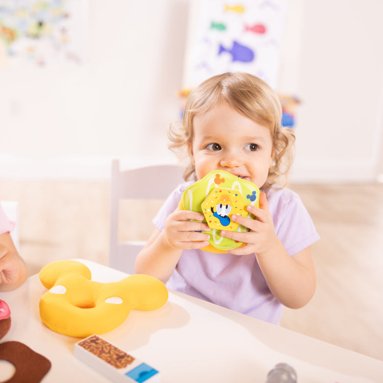 A kid playing with The Melissa & Doug Disney Fill and Top Donut Play Set with 4 Squishy Donuts and Wooden Toppings - For Ages 3+