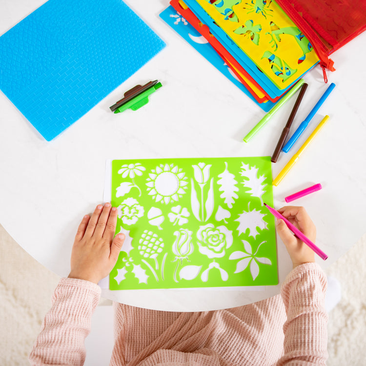 A kid playing with The Melissa & Doug Created by Me! Stencil Art Coloring Activity Kit in Storage Pouch -- 170+ Designs, 6 Markers, 2 Crayons, Paper