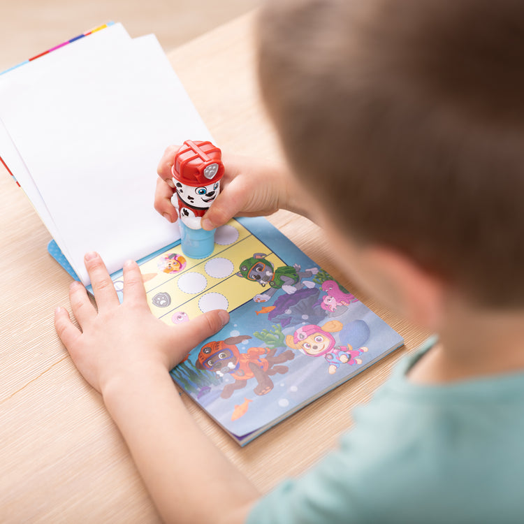 A kid playing with The Melissa & Doug Sticker WOW!™ 24-Page Activity Pad and Sticker Stamper, 300 Stickers, Arts and Crafts Fidget Toy Collectible Character – PAW Patrol Marshall