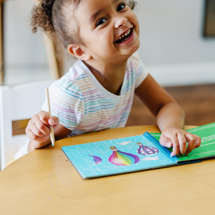 A kid playing with The Melissa & Doug On the Go Scratch Art Hidden-Picture Pad - Favorite Things