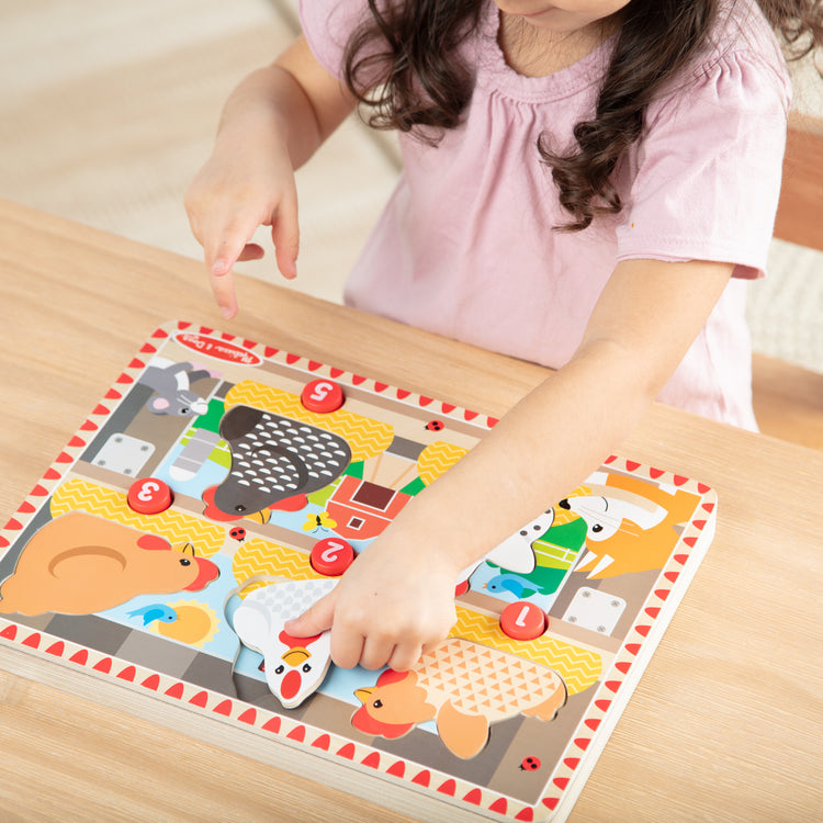 A kid playing with The Melissa & Doug Happy Hens Push to Pop Wooden Puzzle, Montessori-Inspired Toddler Puzzles with Magnetic Pieces and Colorful Puzzle Board, Preschool Toys for Girls & Boys 18 months+