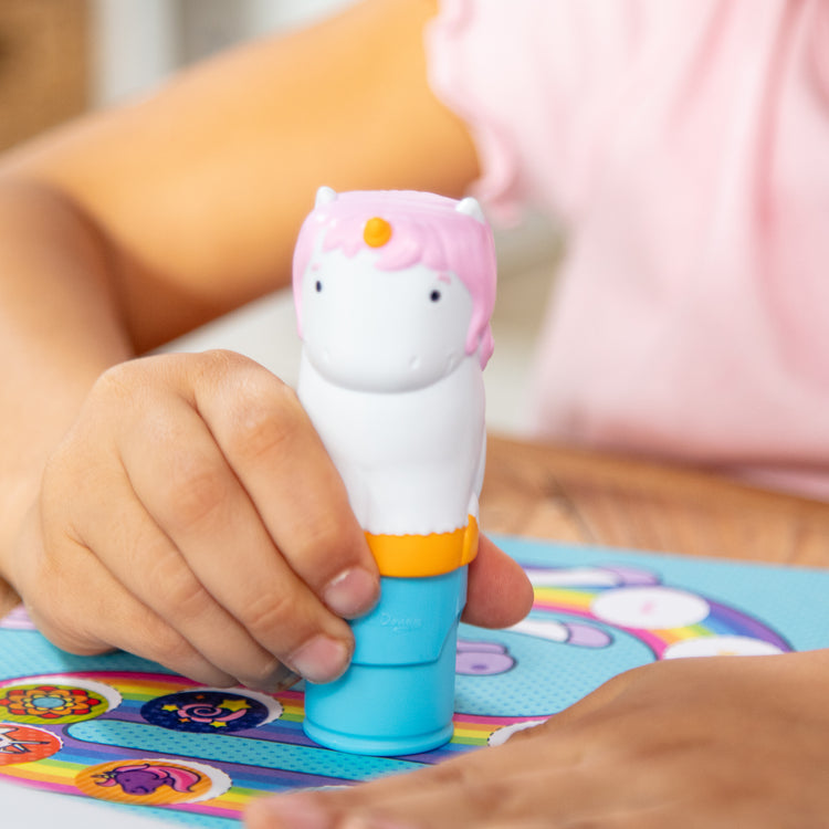 A kid playing with The Melissa & Doug Sticker WOW!™ 24-Page Activity Pad and Sticker Stamper, 300 Stickers, Arts and Crafts Fidget Toy Collectible Character – Unicorn