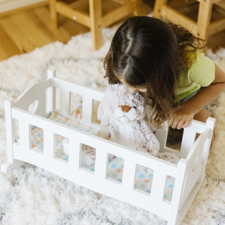 A kid playing with The Melissa & Doug Mine to Love Wooden Play Cradle for Dolls, Stuffed Animals - White