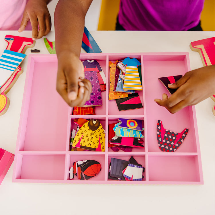 A kid playing with The Melissa & Doug Abby and Emma Deluxe Magnetic Wooden Dress-Up Dolls Play Set (55+ pcs)