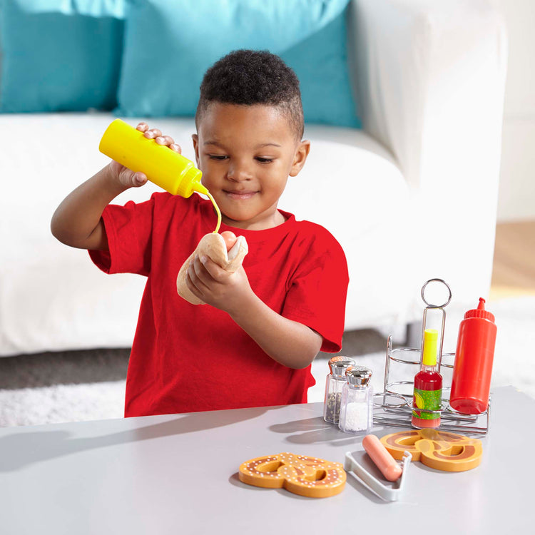 A kid playing with The Melissa & Doug Condiments Play Set (6 pcs) - Play Food, Stainless Steel Caddy