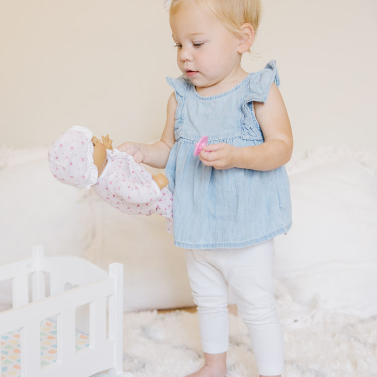 A kid playing with The Melissa & Doug Mine to Love Wooden Play Cradle for Dolls, Stuffed Animals - White