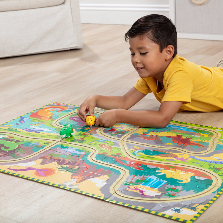A kid playing with The Melissa & Doug Dinosaur Adventure Tracks Cardboard Jigsaw Floor Puzzle and 2 Wind-Up Dinos – 48 Pieces, for Boys and Girls 3+ 