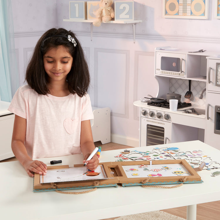 A kid playing with The Melissa & Doug Natural Play: Play, Draw, Create Reusable Drawing & Magnet Kit – Ocean (42 Magnets, 5 Dry-Erase Markers)