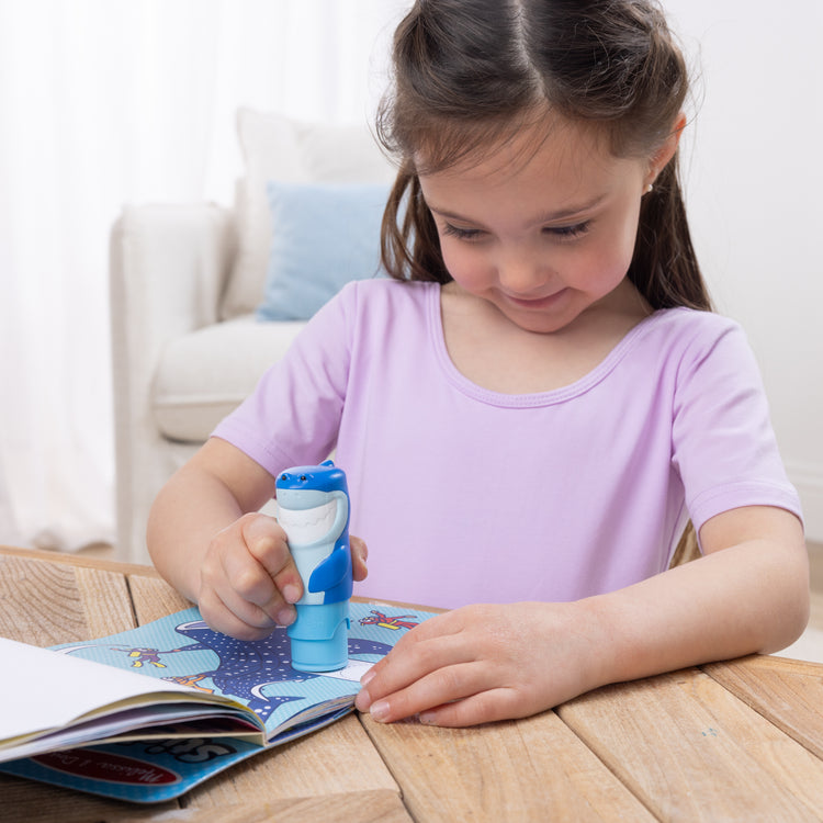 A kid playing with The Melissa & Doug Sticker WOW!™ Shark Bundle: 24-Page Activity Pad, Sticker Stamper, 500 Stickers, Mini Pad, Arts and Crafts Fidget Toy Collectible Character