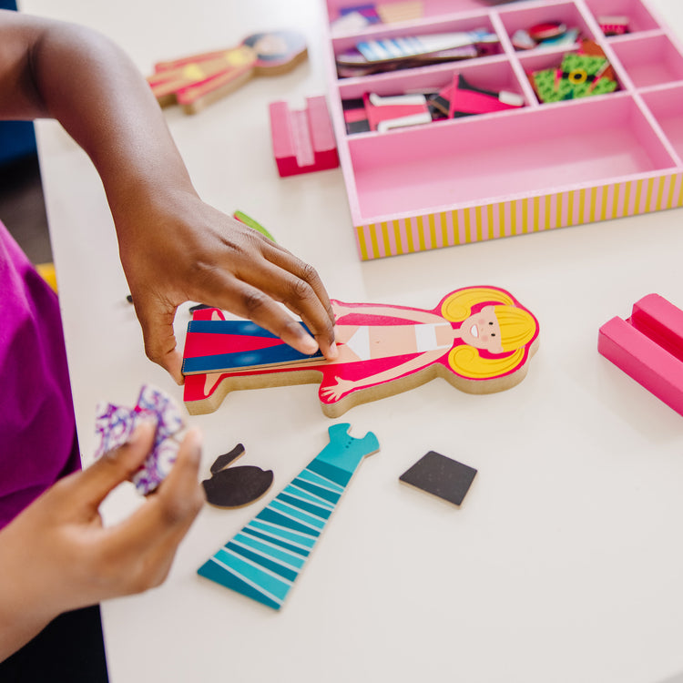 A kid playing with The Melissa & Doug Abby and Emma Deluxe Magnetic Wooden Dress-Up Dolls Play Set (55+ pcs)