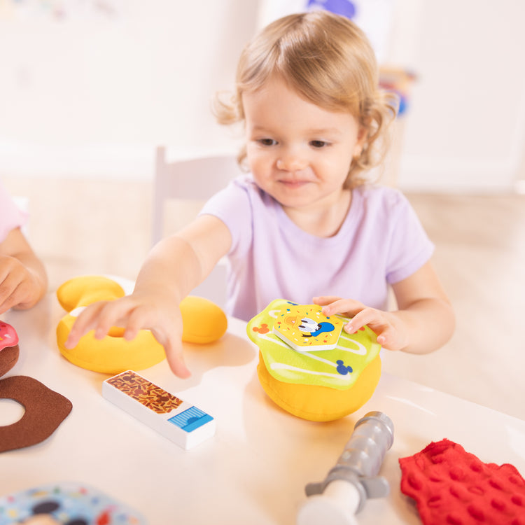 A kid playing with The Melissa & Doug Disney Fill and Top Donut Play Set with 4 Squishy Donuts and Wooden Toppings - For Ages 3+