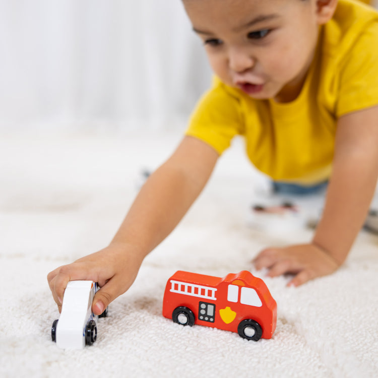 A kid playing with The Melissa & Doug Wooden Town Vehicles Set in Wooden Tray (9 pcs)