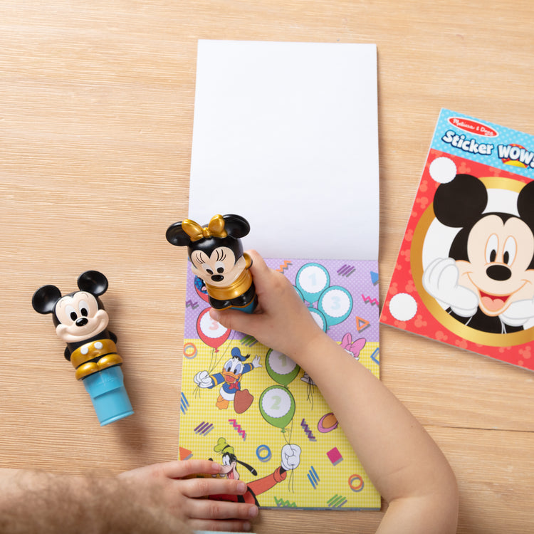 A kid playing with The Melissa & Doug Sticker WOW! Disney Special Edition Pack with Mickey & Minnie Stampers and 900 Stickers - Ages 3+