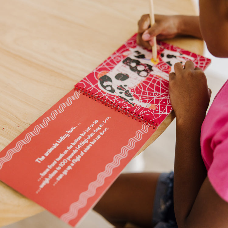 A kid playing with The Melissa & Doug On the Go Scratch Art: Animal Families Hidden-Picture Activity Pad With Stylus