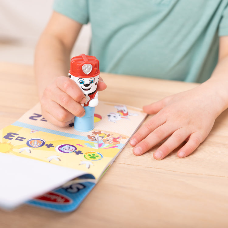A kid playing with The Melissa & Doug Sticker WOW!™ 24-Page Activity Pad and Sticker Stamper, 300 Stickers, Arts and Crafts Fidget Toy Collectible Character – PAW Patrol Marshall