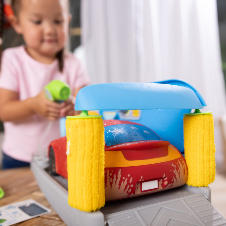 A kid playing with The Melissa & Doug Spray & Shine Car Wash Color-Changing Water Toy Play Set Boys and Girls 3+