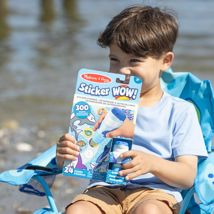 A kid playing with The Melissa & Doug Sticker WOW!™ Shark Bundle: 24-Page Activity Pad, Sticker Stamper, 500 Stickers, Mini Pad, Arts and Crafts Fidget Toy Collectible Character