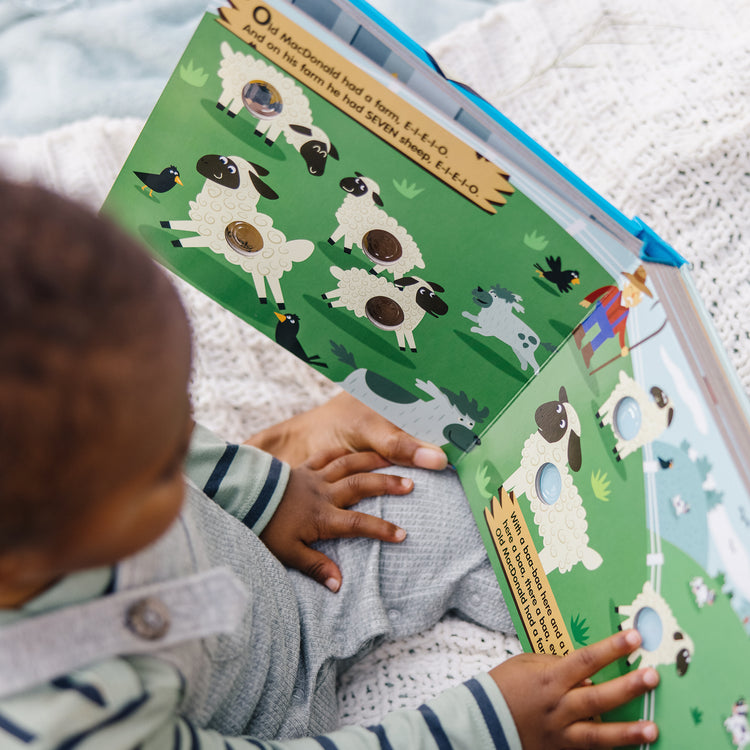 A kid playing with The Melissa & Doug Children's Book - Poke-a-Dot: Old MacDonald’s Farm (Board Book with Buttons to Pop)