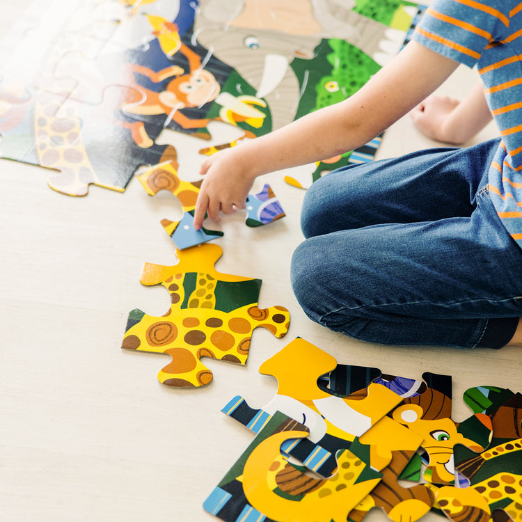 A kid playing with The Melissa & Doug Safari Social Jumbo Jigsaw Floor Puzzle (24 pcs, 2 x 3 feet)