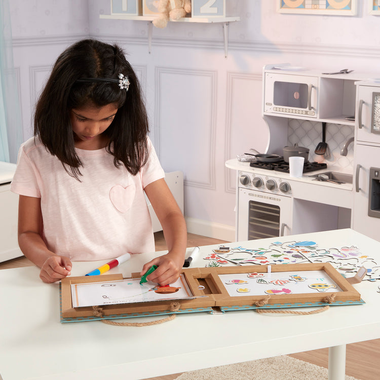 A kid playing with The Melissa & Doug Natural Play: Play, Draw, Create Reusable Drawing & Magnet Kit – Ocean (42 Magnets, 5 Dry-Erase Markers)