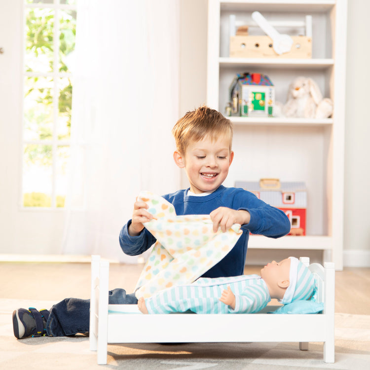 A kid playing with The Melissa & Doug Mine to Love Wooden Play Bed for Dolls, Stuffed Animals - White (8.7”H x 9.1”W x 20.7”L Assembled)