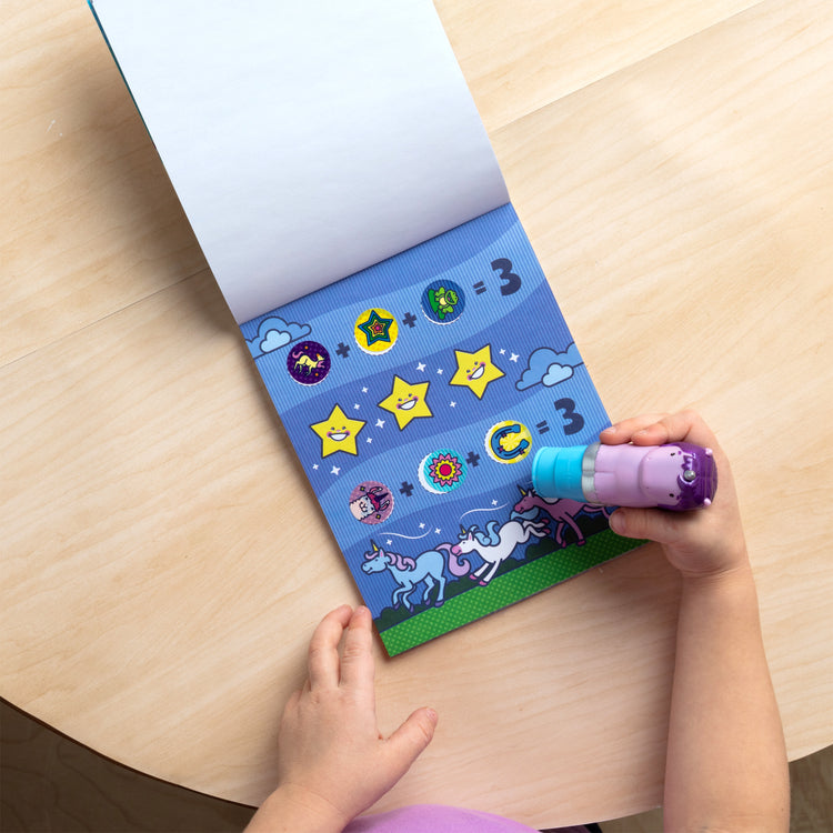 A kid playing with The Melissa & Doug Sticker WOW!™ 24-Page Activity Pad and Sticker Stamper, 300 Stickers, Arts and Crafts Fidget Toy Collectible Character – Sprinkles the Purple Unicorn