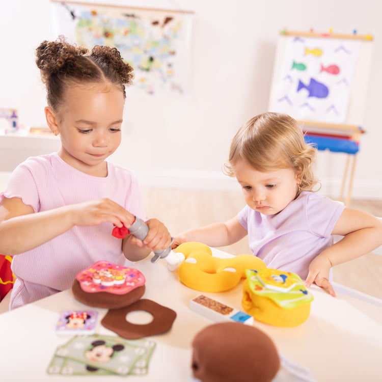 A kid playing with The Melissa & Doug Disney Fill and Top Donut Play Set with 4 Squishy Donuts and Wooden Toppings - For Ages 3+