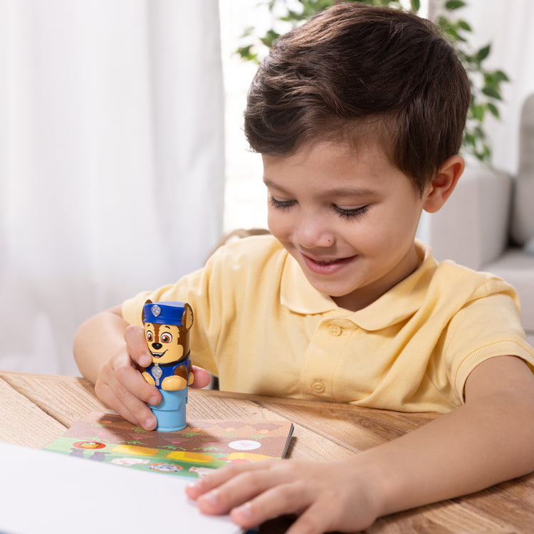 A kid playing with The Melissa & Doug Sticker WOW!™ 24-Page Activity Pad and Sticker Stamper, 300 Stickers, Arts and Crafts Fidget Toy Collectible Character – PAW Patrol Chase
