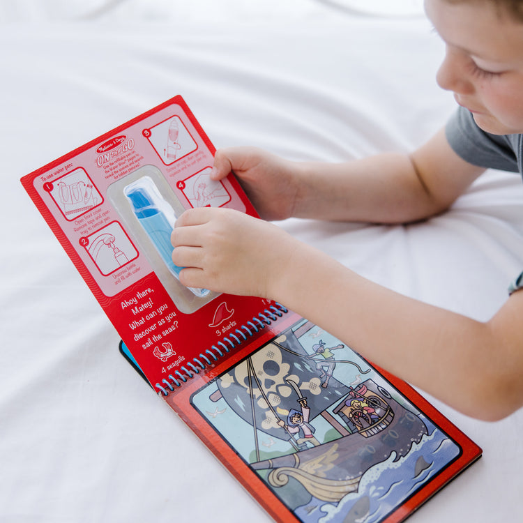 A kid playing with The Melissa & Doug On the Go Water Wow! Reusable Water-Reveal Activity Pad Travel Toy – Adventure