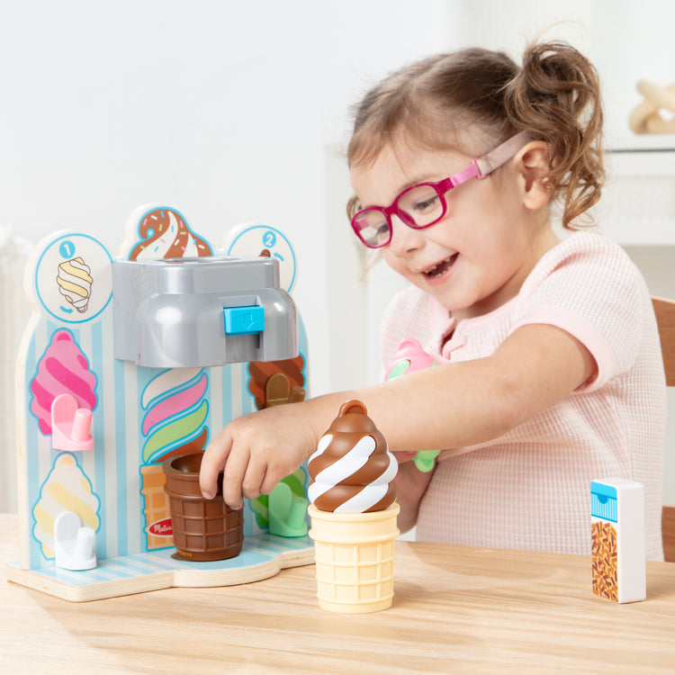 A kid playing with The Melissa & Doug Swirl and Serve Wooden Ice Cream Play Set with Dispenser and 4 Swirls - For Ages 3+
