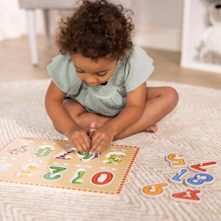 A kid playing with The Melissa & Doug Lift & See Numbers Wooden Peg Puzzle - 10 Pieces