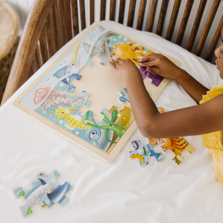 A kid playing with The Melissa & Doug Under the Sea Ocean Animals Wooden Jigsaw Puzzle With Storage Tray (24 pcs)