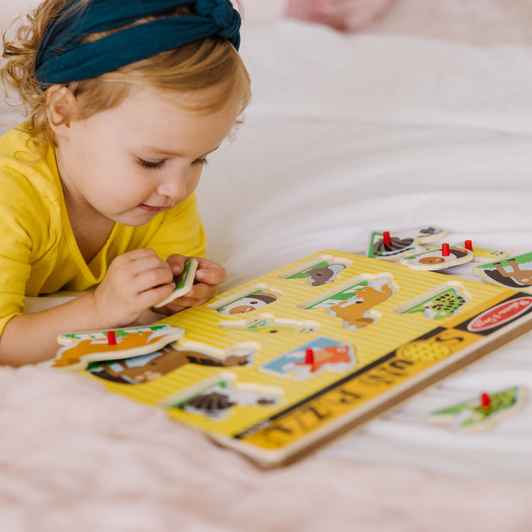 A kid playing with The Melissa & Doug Pets Sound Puzzle - Wooden Peg Puzzle With Sound Effects (8 pcs)