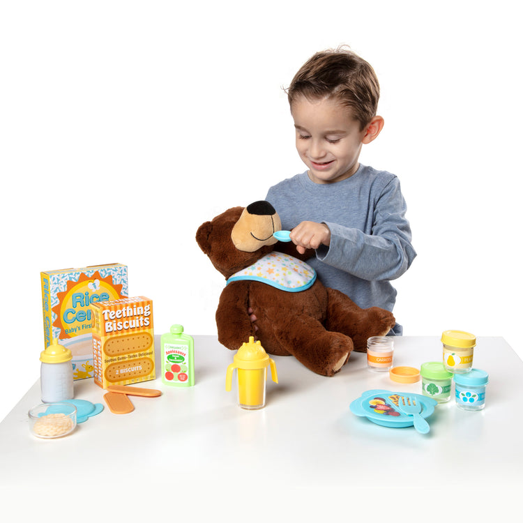 A child on white background with The Melissa & Doug Mine to Love Mealtime Play Set for Dolls with Bottle, Pretend Baby Food Jars, Snack Pouch, More (24 pcs)