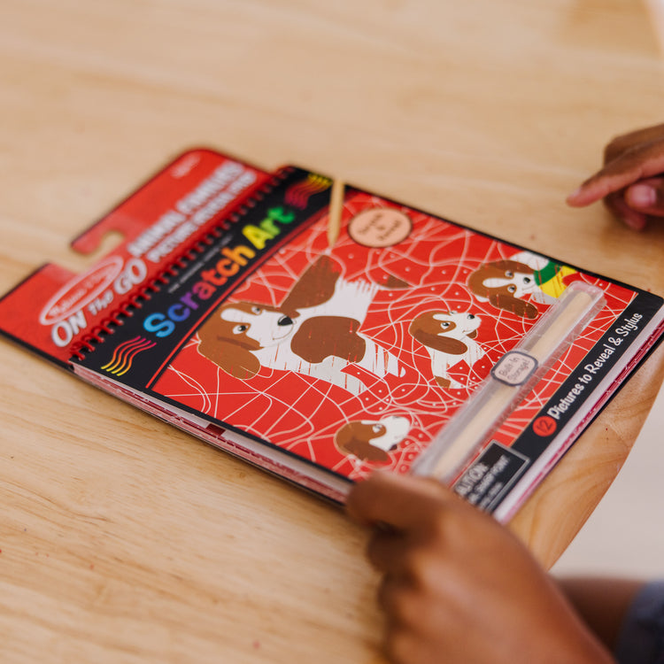 A kid playing with The Melissa & Doug On the Go Scratch Art: Animal Families Hidden-Picture Activity Pad With Stylus