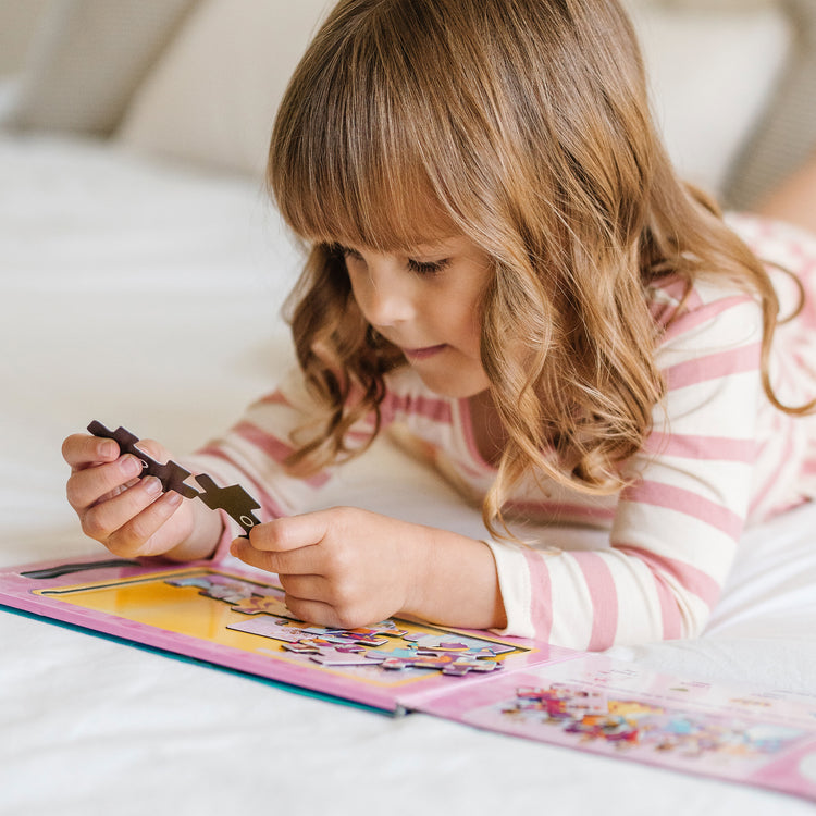 A kid playing with The Melissa & Doug Take-Along Magnetic Jigsaw Puzzles Travel Toy – Princesses (2 15-Piece Puzzles)