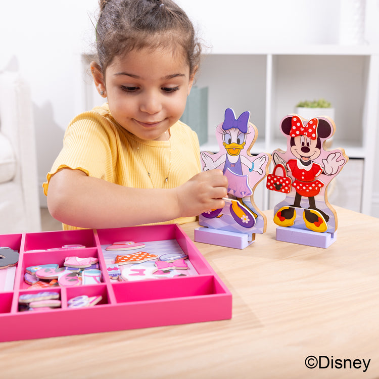A kid playing with The Melissa & Doug Disney Minnie Mouse and Daisy Duck Deluxe Wooden Magnetic Dress-Up; 2 Fashion Dolls with Stands for Pretend Play, 52 Pieces
