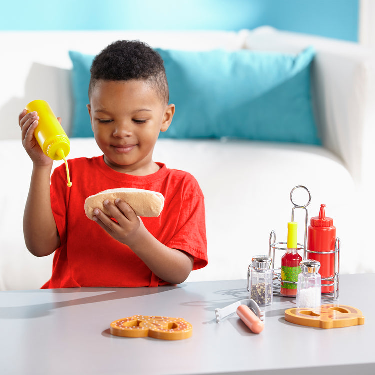 A kid playing with The Melissa & Doug Condiments Play Set (6 pcs) - Play Food, Stainless Steel Caddy