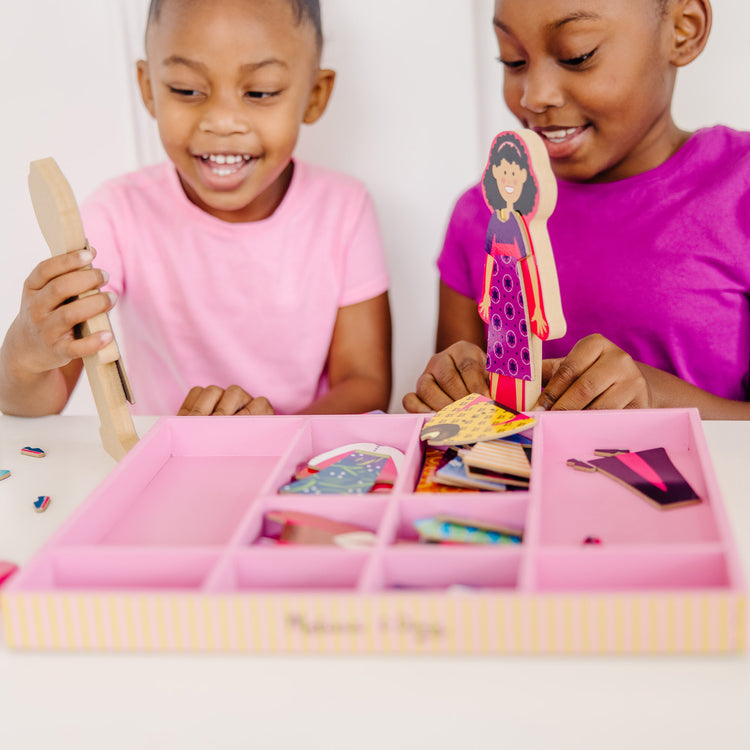 A kid playing with The Melissa & Doug Abby and Emma Deluxe Magnetic Wooden Dress-Up Dolls Play Set (55+ pcs)