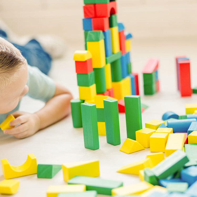 A kid playing with the Melissa & Doug Wooden Building Block Set - 200 Blocks in 4 Colors and 9 Shapes
