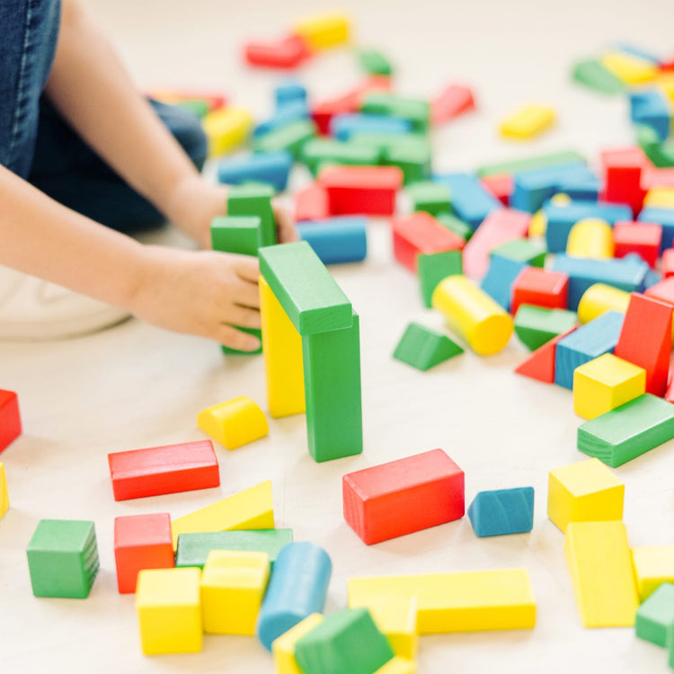 A kid playing with the Melissa & Doug Wooden Building Block Set - 200 Blocks in 4 Colors and 9 Shapes
