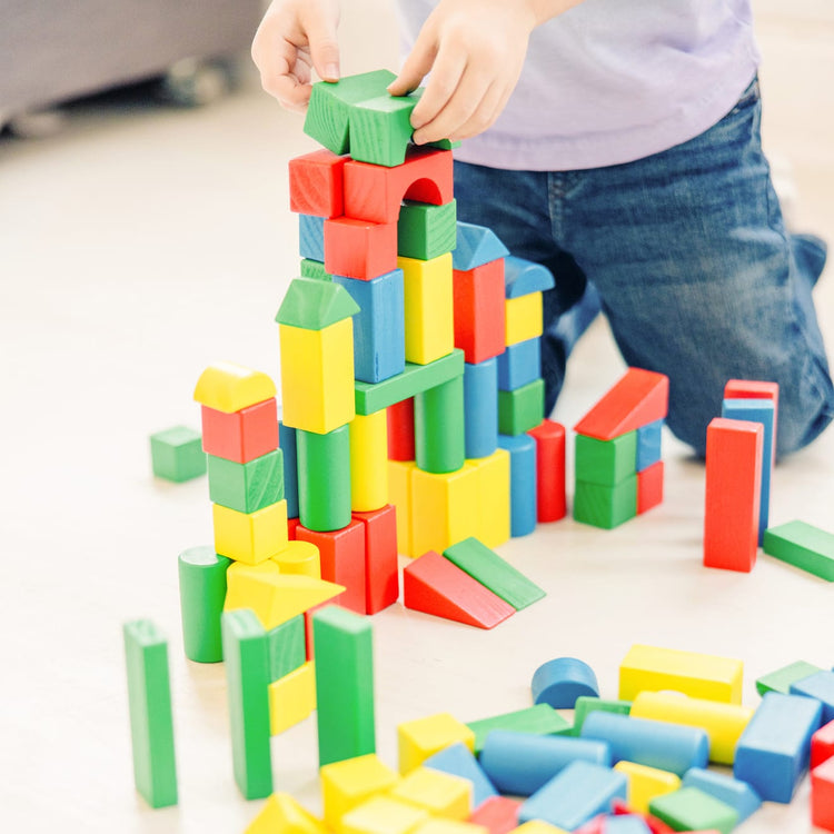 A kid playing with the Melissa & Doug Wooden Building Block Set - 200 Blocks in 4 Colors and 9 Shapes