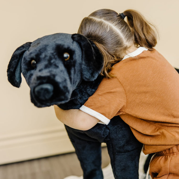 A kid playing with the Melissa & Doug Giant Black Lab - Lifelike Stuffed Animal Dog (over 2 feet tall)