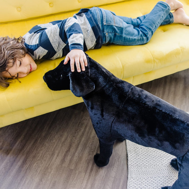 A kid playing with the Melissa & Doug Giant Black Lab - Lifelike Stuffed Animal Dog (over 2 feet tall)