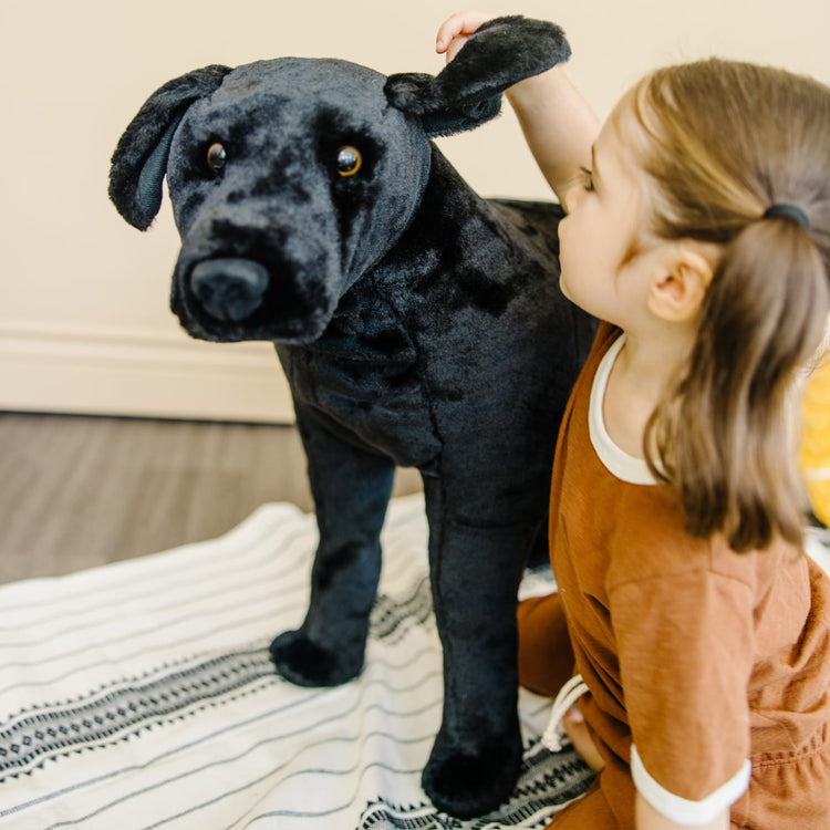 A kid playing with the Melissa & Doug Giant Black Lab - Lifelike Stuffed Animal Dog (over 2 feet tall)