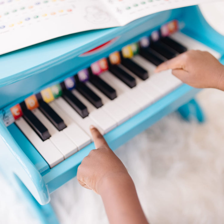 A kid playing with the Melissa & Doug Learn-to-Play Piano With 25 Keys and Color-Coded Songbook - Blue