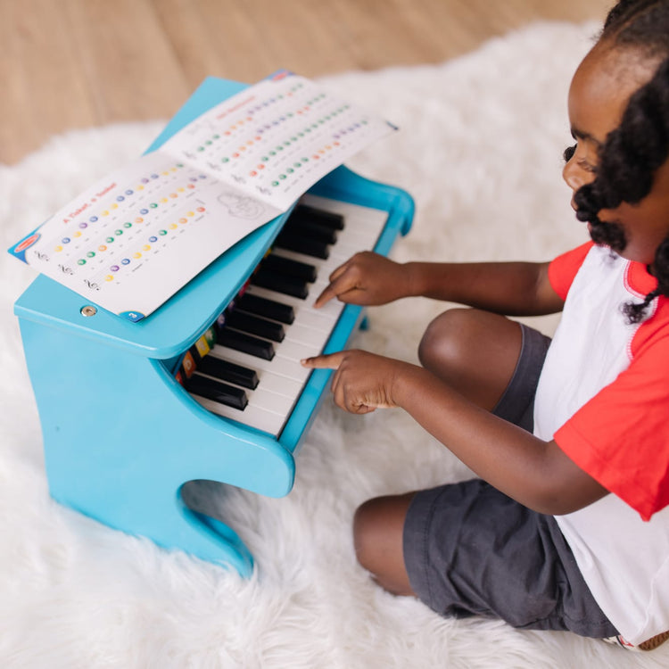 A kid playing with the Melissa & Doug Learn-to-Play Piano With 25 Keys and Color-Coded Songbook - Blue