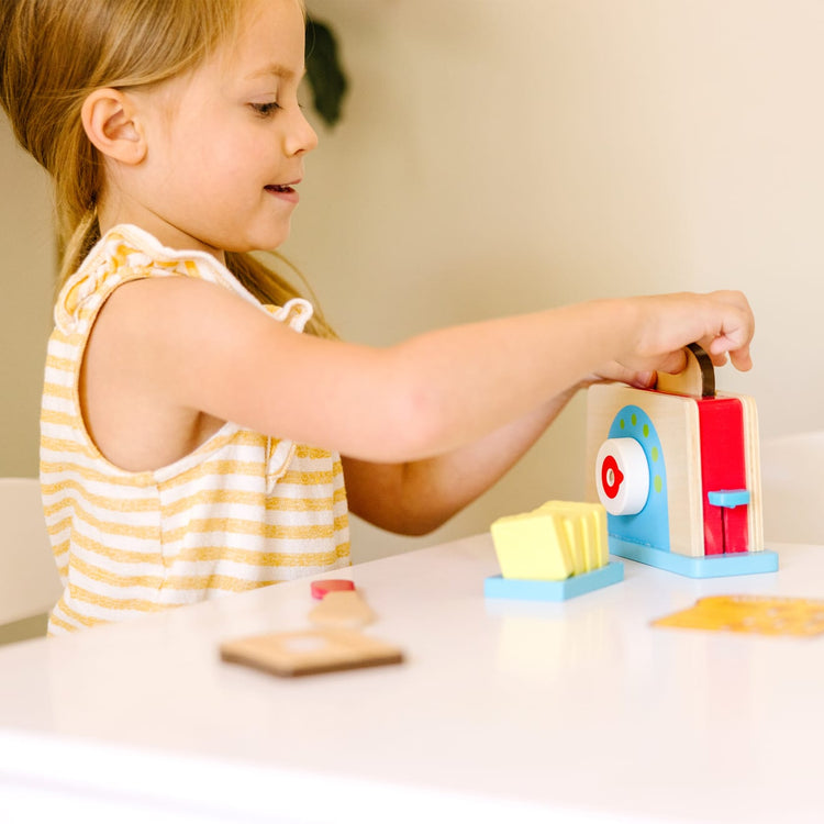 A kid playing with the Melissa & Doug Bread and Butter Toaster Set (9 pcs) - Wooden Play Food and Kitchen Accessories