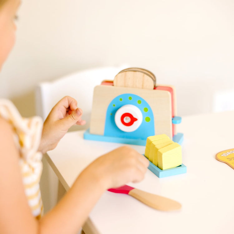 A kid playing with the Melissa & Doug Bread and Butter Toaster Set (9 pcs) - Wooden Play Food and Kitchen Accessories