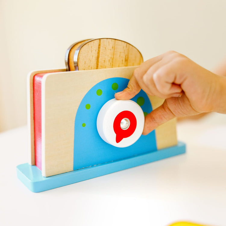 A kid playing with the Melissa & Doug Bread and Butter Toaster Set (9 pcs) - Wooden Play Food and Kitchen Accessories